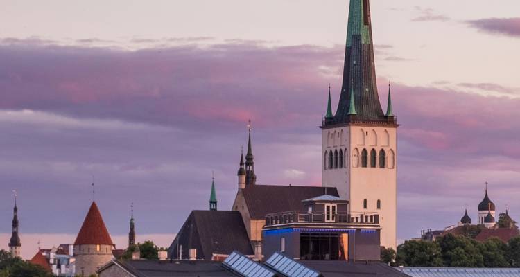 Tallinn skyline at pastel sunset with St. Olaf’s Church spire rising above historic rooftops.