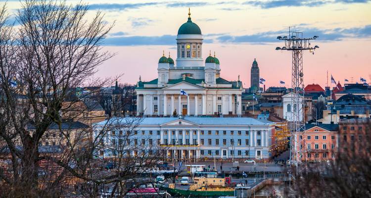Distant view of Helsinki Cathedral framed by trees and city rooftops at soft evening light.