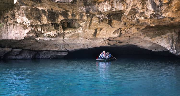Una pequeña barca con visitantes se desliza hacia una cueva de piedra caliza sobre aguas turquesas cristalinas.