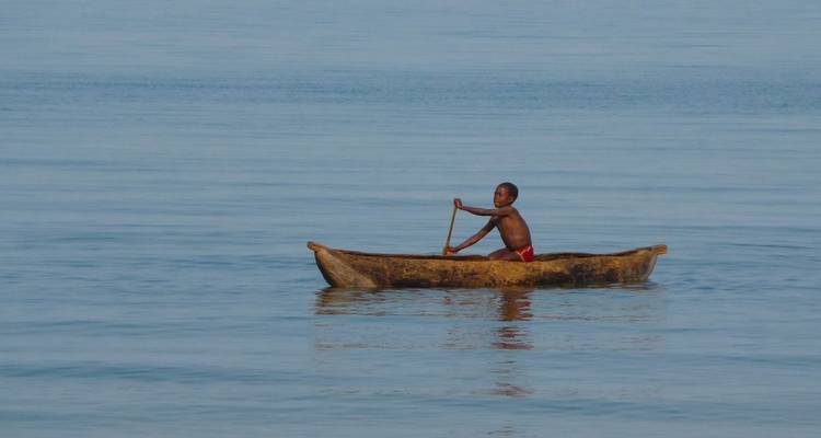 Kind paddelt in kleinem hölzernem Kanu auf der spiegelglatten blauen Oberfläche des Malawi-Sees