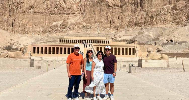 Un groupe de quatre personnes se tient sur la grande esplanade menant au Temple en terrasses d'Hatchepsout creusé dans une falaise imposante.