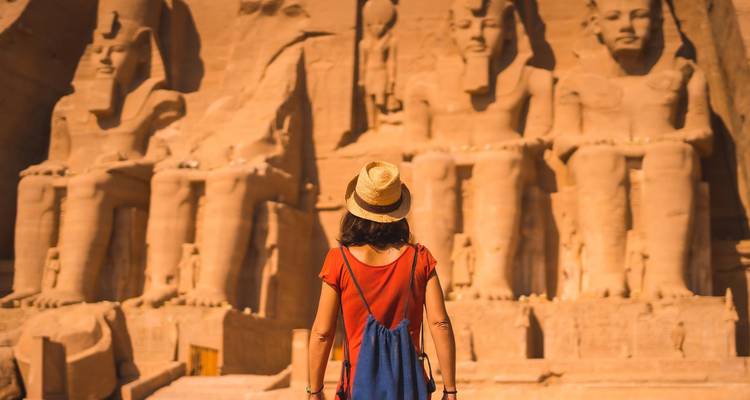 Voyageur au chapeau de paille admirant les colossales statues assises d'Abu Simbel baignées par la lumière chaude du soleil.