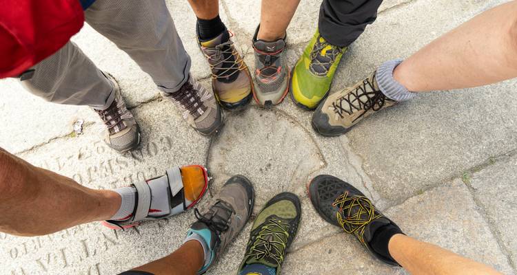 Cirkel van versleten wandelschoenen die met hun punten elkaar raken op een stenen oppervlak, als symbool van Camino-teamwork.