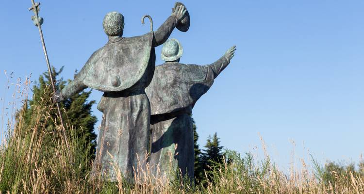 Bronzen beeld van twee blijde pelgrims die hun armen naar de hemel heffen te midden van hoog gras.