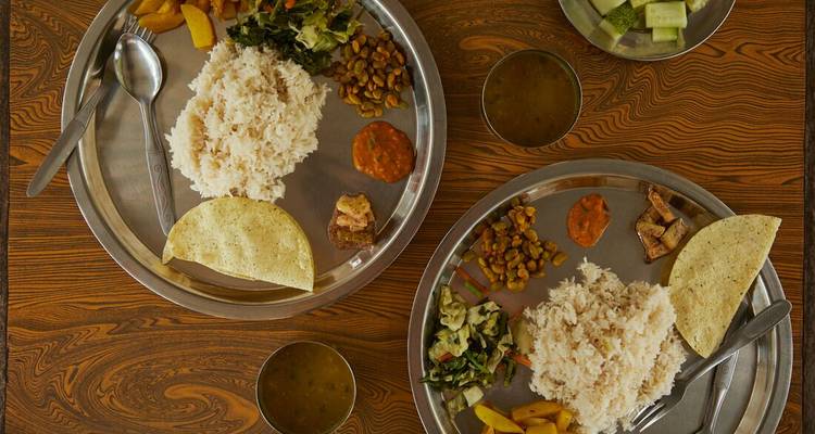 Two metal trays of rice, curried vegetables and dal on a wooden table.