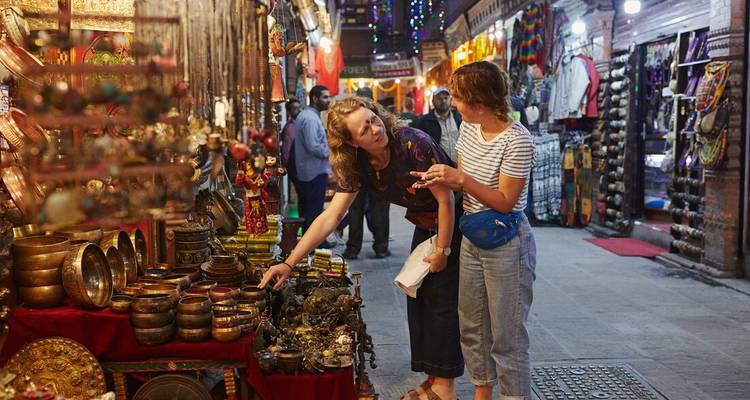 Travellers browsing brass bowls and souvenirs in a vibrant Kathmandu night market.