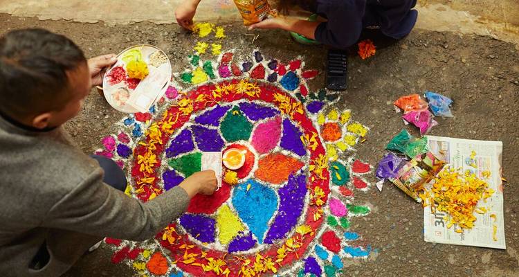 Creating a colourful flower petal rangoli design on the ground during a festival.