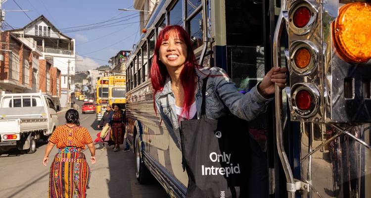 Une jeune femme se penche d'un autobus guatémaltèque coloré en souriant dans une rue animée.