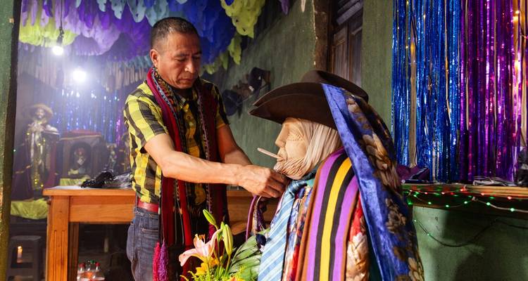 Local man arranging garments on the folkloric effigy of Maximon inside a festive shrine.