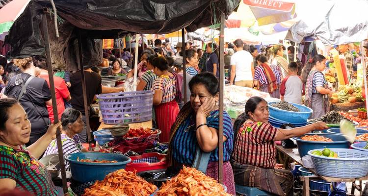 Marché traditionnel animé rempli de résidents vêtus de vêtements tissés colorés achetant des produits frais.