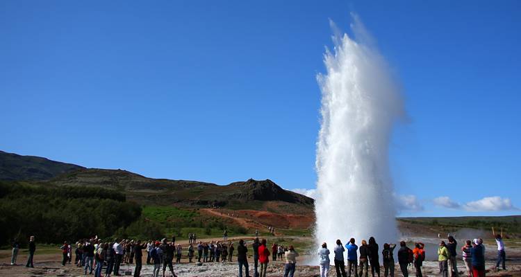 Crowd of tourists watching a powerful geyser burst against a clear blue Icelandic sky.