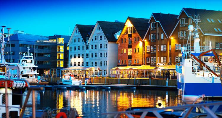 Avondscène aan het water met traditionele houten pakhuizen die verlicht zijn naast aangemeerde boten.