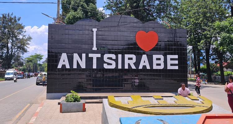 Cartel grande en la ciudad que dice 'I ♥ Antsirabe' en una calle concurrida con gente local cerca.