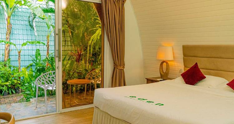 Habitación luminosa del resort con vista al jardín a través de una puerta corredera de vidrio, paredes blancas y cama perfectamente hecha.