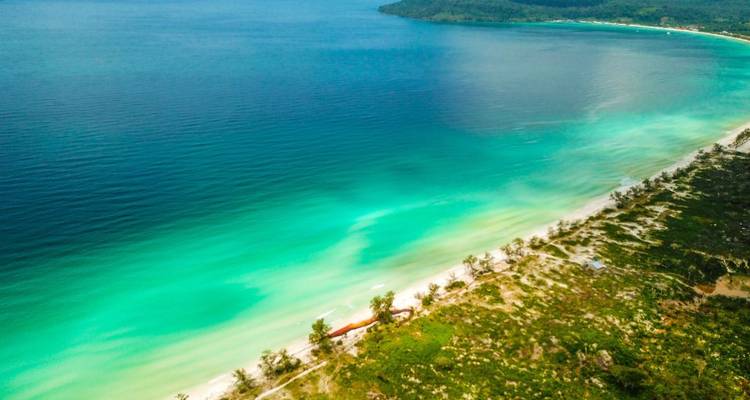 Vista aérea de una costa prístina con aguas turquesas vividas que se desvanecen en el mar azul profundo y un promontorio boscoso.