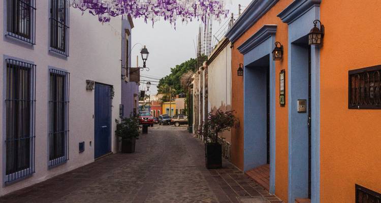 Enge Kopfsteinpflaster-Gasse, gesäumt von farbenfrohen Fassaden und hängenden violetten Dekorationen.