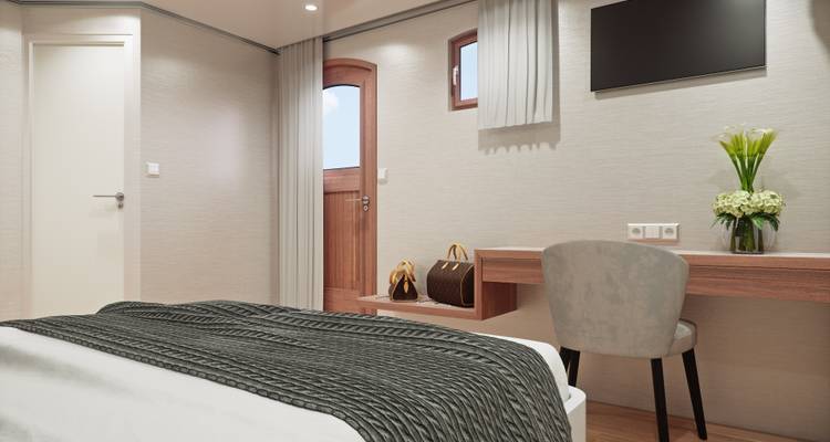 Interior de cabaña con escritorio, silla, ventana y una cama bien arreglada a bordo de un crucero.