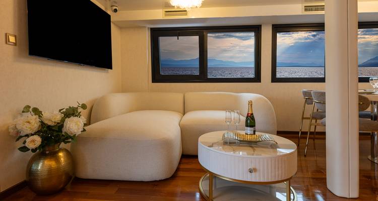 Acogedor rincón interior con sofá moderno, champagne sobre una mesita de café y vistas al mar a través de grandes ventanas.