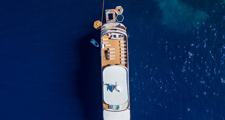 Close top-down crop of yacht sun deck with loungers and floating platforms attached on deep blue water.