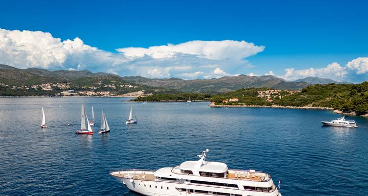 Bay scene with multiple small sailboats and partial view of a yacht’s top deck under vibrant blue sky with cumulus clouds.