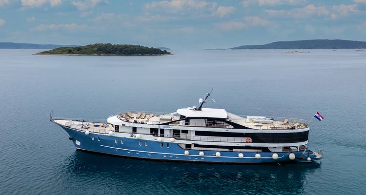 Yacht de luxe près de petites îles croates sous un ciel partiellement nuageux avec drapeau national flottant