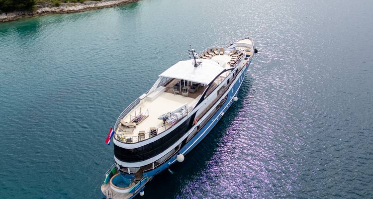 Vue aérienne d'un yacht bleu et blanc élégant ancré dans une mer turquoise cristalline avec la lumière du soleil se reflétant sur l'eau