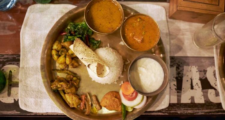 Comida thali nepalí tradicional con arroz, curries y condimentos servidos en una bandeja de latón.