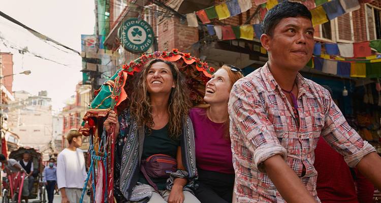 Los turistas pasean en un colorido rickshaw de ciclo por una animada calle de Katmandú decorada con banderas de oración.