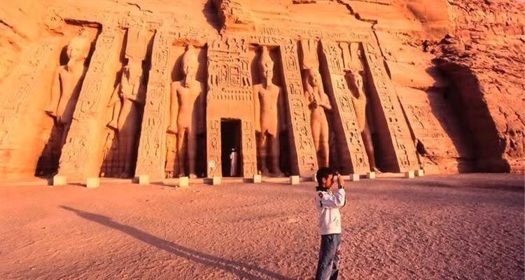 Bezoeker fotografeert de in rots uitgehouwen tempelgevel van Abu Simbel in het gouden licht van de zonsondergang