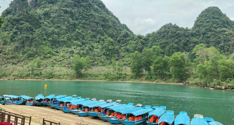 Rangée de bateaux touristiques bleus amarrés sur une rivière émeraude entourée de montagnes calcaires aux pentes escarpées couvertes de jungle.