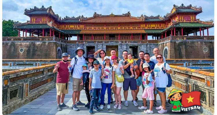 Un groupe de touristes pose devant la porte de la Cité impériale à Hue avec le logo de dessin animé du Vietnam en bas.