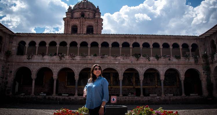 Un visiteur se tient dans la cour d'un cloître historique doté de balcons voûtés et de massifs de fleurs.