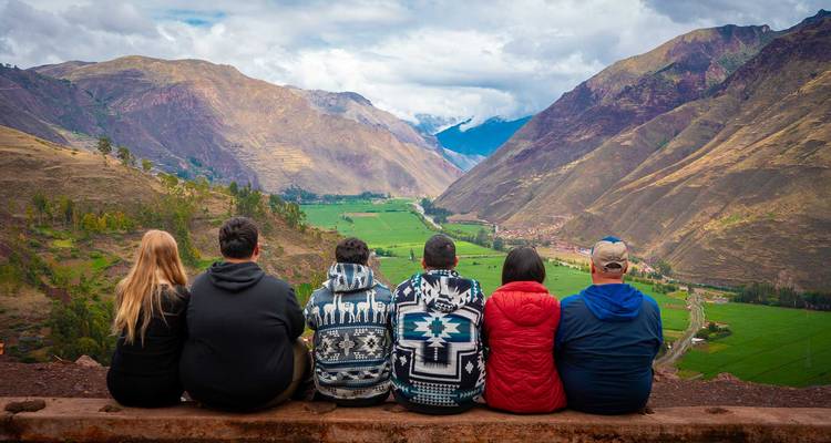 Groupe de voyageurs assis sur un rebord surplombant la luxuriante Vallée Sacrée et les pics imposants.