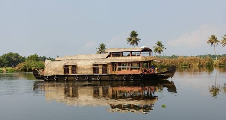 Traditionelles Hausboot mit Strohdach, das sich perfekt in den ruhigen Backwaters von Kerala spiegelt.