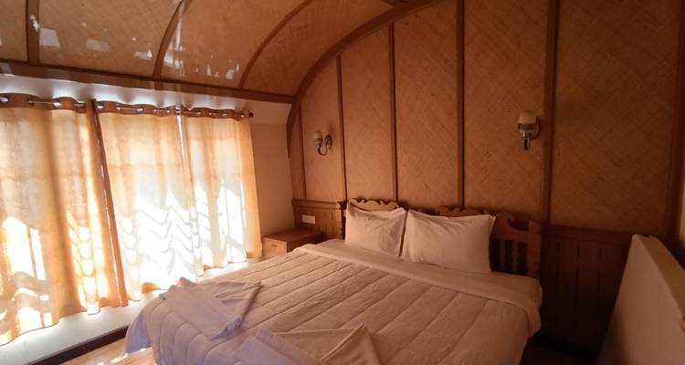 Gemütliches Schlafzimmer einer Berghütte mit großem Bett, Holzvertäfelung und sanftem Naturlicht durch die Vorhänge.