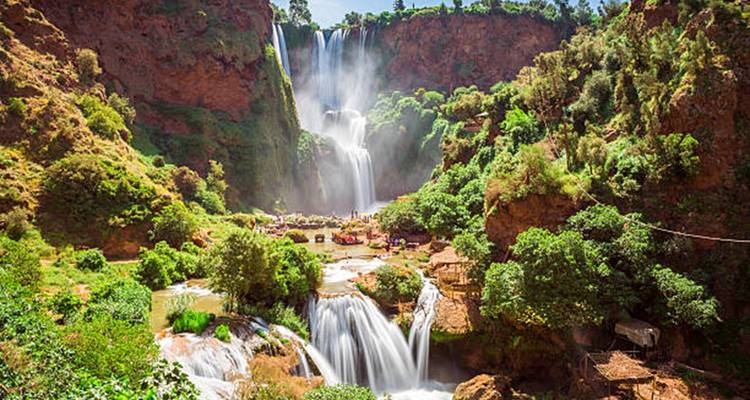 Vista panorámica de las cascadas escalonadas de Ouzoud rodeadas de frondosa vegetación bajo un sol radiante