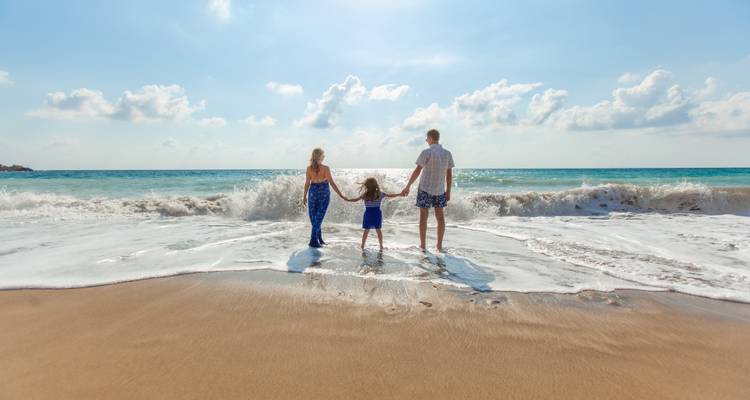 Een gezin dat elkaar aan de hand houdt staat aan de waterkant terwijl golven op een zonnig Cypriotisch strand neerkomen.