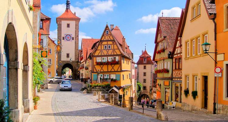 Sprookjesachtige steeg van Rothenburg ob der Tauber met vakwerkhuizen en middeleeuwse toren onder blauwe lucht.