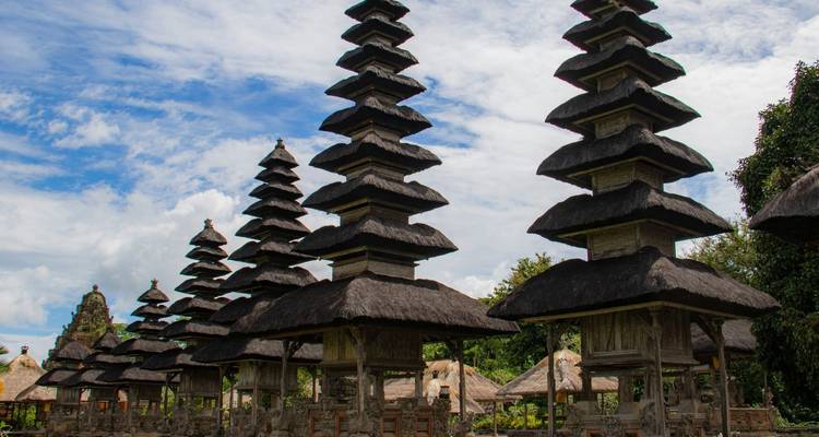 Tall thatched meru towers dominate a Balinese temple courtyard against a backdrop of blue sky.