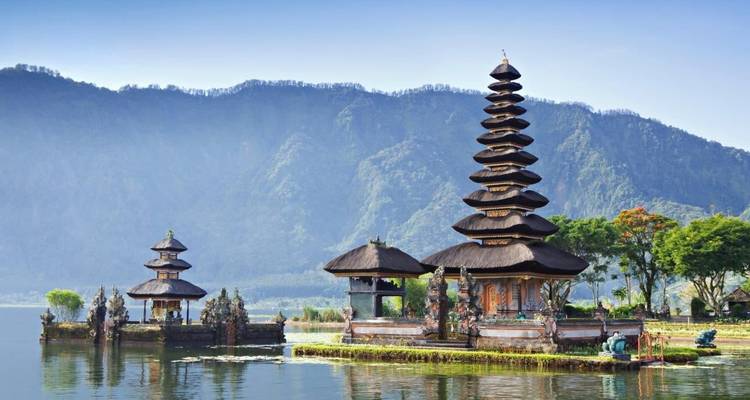 Ulun Danu Beratan temple complex sits on tranquil lake waters with misty mountains behind.