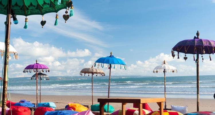 Colorful parasols and beanbags decorate a sandy beach facing gentle ocean waves.