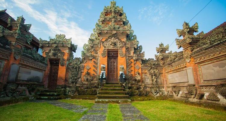 An elaborately carved Balinese temple courtyard with mossy stone steps leads to a central doorway.