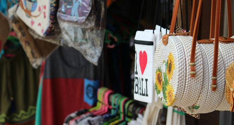 Close-up of woven handbags and an "I ♥ Bali" tote hanging in a local market stall.