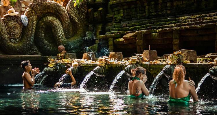 Visitors participate in ritual bathing at a sacred Balinese water temple with ornate stone carvings.