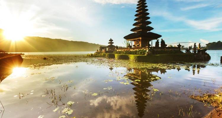 Ein ruhiger Sees-Tempel mit mehrschichtigen Dachpagoden, die sich im ruhigen Wasser spiegeln, während die Sonne hinter fernen Hügeln aufgeht.