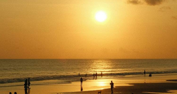 Silhouetten von Strandbesuchern gehen bei einem leuchtend orangefarbenen Sonnenuntergang entlang der Küstenlinie spazieren.