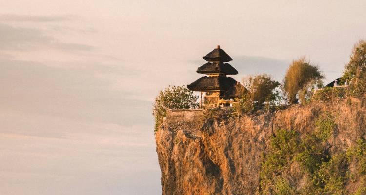 Ein auf einer Klippe gelegener Tempel blickt während der goldenen Stunde auf den Ozean hinab und ist in warmes Licht getaucht.