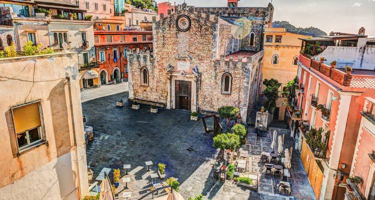 Stenen kathedraal en levendig plein in Taormina omgeven door kleurrijke historische gebouwen.