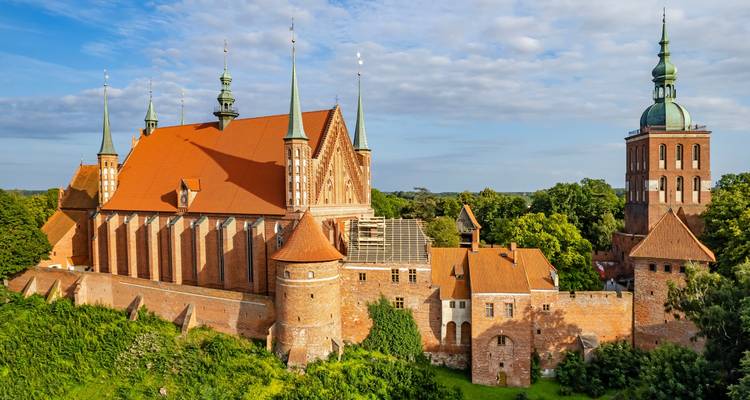 Frombork Cathedral complex with soaring green-topped towers and red-tile roofs set amid lush greenery.