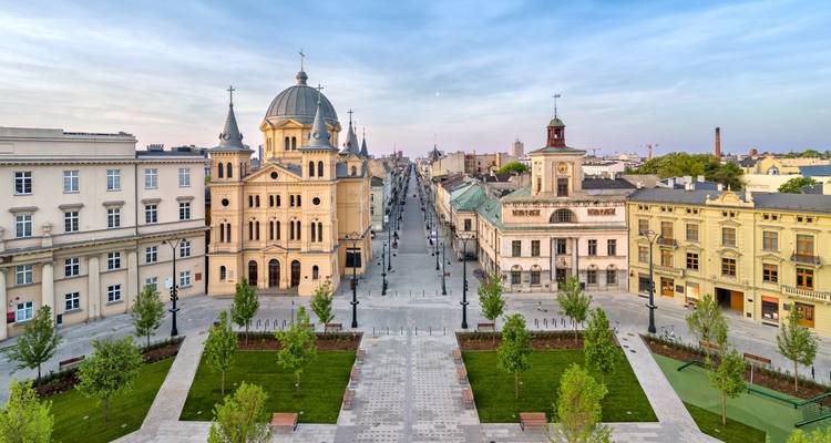 Panoramic view along Łódź’s Piotrkowska Street showcasing historic architecture, a domed church and tree-lined promenade.
